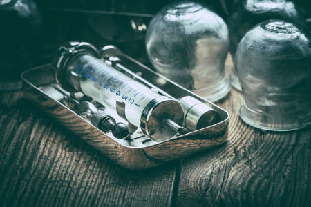 Retro syringe, stethoscope and medical cupping glass on a wooden table. Shallow depth of field. Filtered style.の写真素材