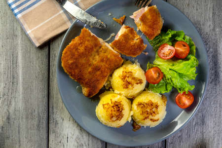 Cutlet cordon bleu with pork ham served with boiled potato and salad on a plate. Top view.