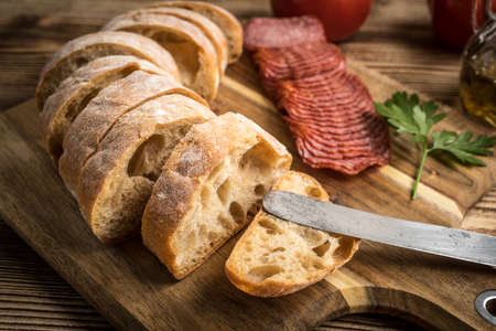 Italian ciabatta bread cut in slices on wooden chopping board with salami.の写真素材