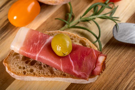 Thinly sliced German black forest ham with sliced ciabatta bread, tomato and olives.