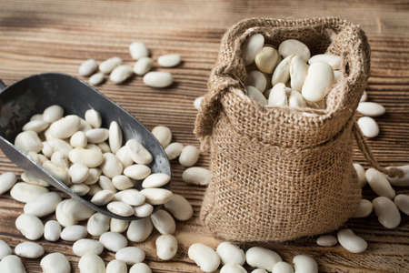 White bean in a jute bag on a wooden table.