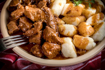 Chunky beef stew with savory sauce beside potato dumplings.