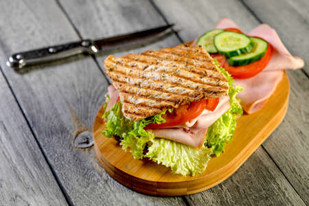 Sandwich with ham, cucumber, tomato and lettuce, with two layers of filling between three slices of toast.の写真素材