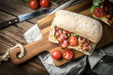 Ciabatta sandwich with arugula salad, bacon and yellow cheese on wooden board. Top view.の写真素材