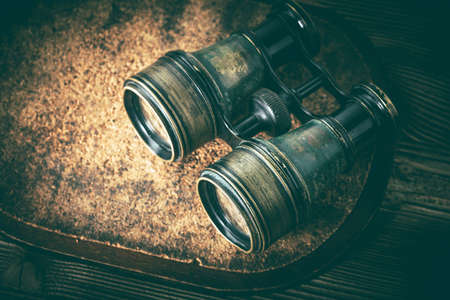 Old binoculars covered with patina on wooden background.の写真素材
