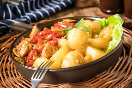 Fried pieces of chicken with red peppers and onions, served with potatoes.の写真素材