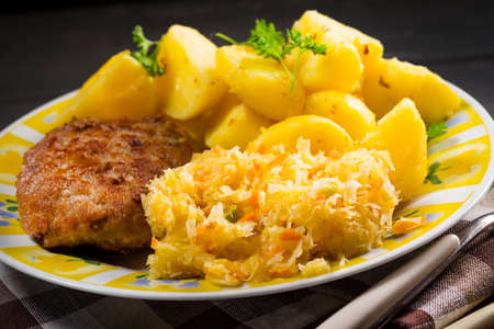 Minced pork cutlet served with potatoes and sauerkraut salad.