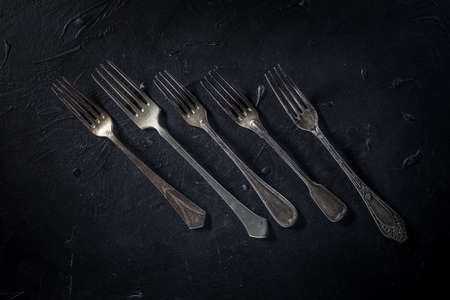 A few old silver forks on dark countertop.