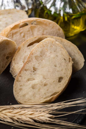 Italian ciabatta bread cut in slices on stone chopping board over dark backdrop.の写真素材