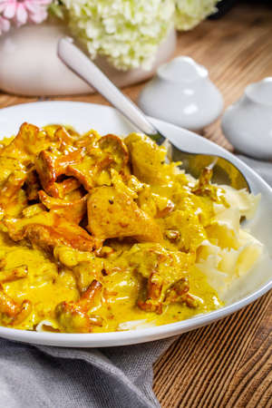 Pasta with fried chicken in cream and chanterelle sauce on wooden table.の写真素材
