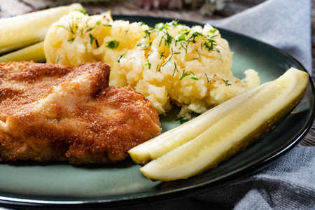 Pork chop served with mashed potatoes and pickled cucumber on plate.