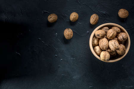 Walnuts in a wooden bowl on a dark background.
