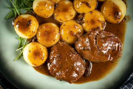 Traditional German braised pork cheeks in brown sauce with mushroom served with silesian dumplings.