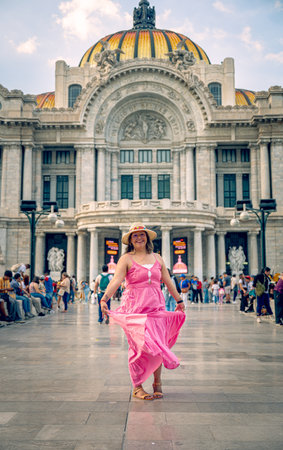 Elegant middle-aged woman in pink dress exploring Mexico City near Torre Latinoamericana, captured by Palacio de Bellas Artes with modern skyline and historic sculpture in the background.の写真素材