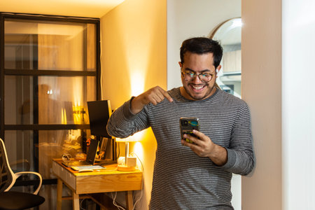 Surprised Man Reading Unexpected News on Smartphone at Homeの写真素材