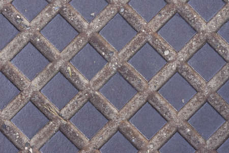 Old dark metal manhole texture with square pattern, background macro, selective focus.