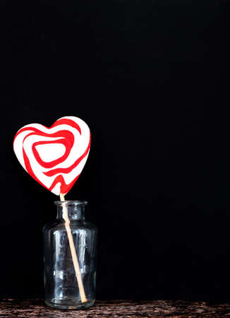 Heart-shaped lollypop in a glass jar against black background, Valentine's Day concept, copy spaceの写真素材