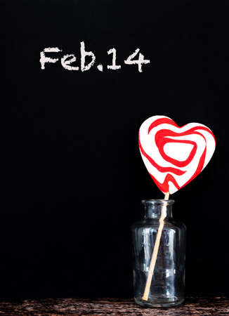 Heart-shaped lollypop in a glass jar against black background with chalk lettering. Valentine's Day concept, copy spaceの写真素材