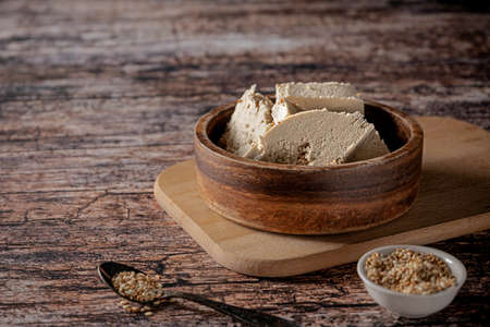 Pieces of tahini halva in a bowl on vintage wooden background, with sesame seeds as its main ingredientの写真素材