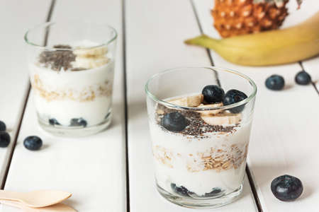 Two glasses with layered yogurt, oats and fruits, on white wooden table. Healthy breakfast, healthy lifestyle conceptの写真素材