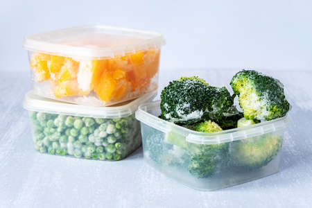 Frozen vegetables. Frozen broccoli, peas and pumpkin in plastic boxes on gray tableの写真素材