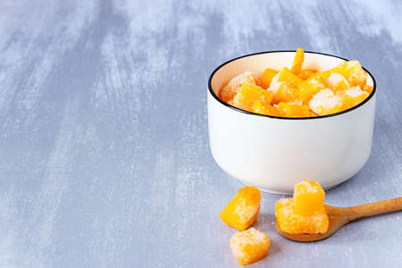 Frozen pieces of pumpkin in a white bowl and a wooden spoon on gray table, copy spaceの写真素材