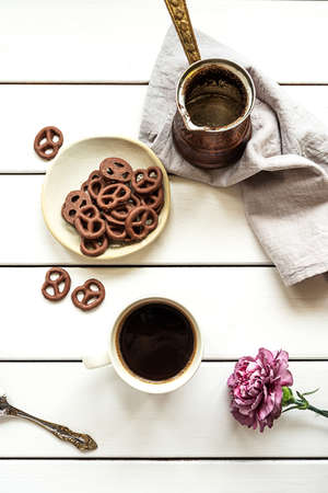 Top view of a cup of coffee, empty coffee pot, chocolate-covered pretzels and a flower on a white wooden background. Breakfast or coffee break composition.の写真素材