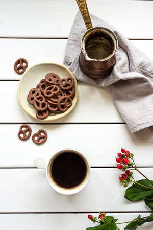 Top view of a cup of coffee, coffee pot and chocolate-covered pretzels on a white wooden background. Breakfast or coffee break composition.の写真素材