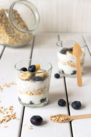 Two glasses with layered yogurt, oats and fruits, on white wooden tableの写真素材