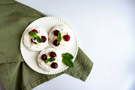 Meringue cakes decorated with whipped cream, cherries and mint leaves on a white plate and green napkin, top view with copy spaceの写真素材