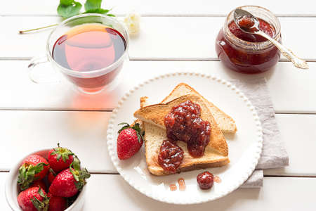 Toasted bread slices with strawberry jam and a jar of jamの写真素材