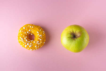 A donut and an apple on pink and yellow background. Diet concept.の写真素材