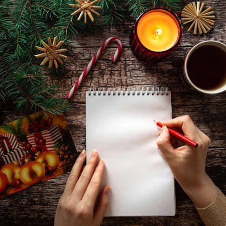 Womans hand writing on a blank notepad sheet in Christmas settingの写真素材