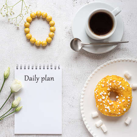 A notepad for daily planning with breakfast setting on gray concrete background. A cup of coffee, donut, flowers and a wooden bracelet. Concept of a lady's daily planning, work, study. Copy space.の写真素材