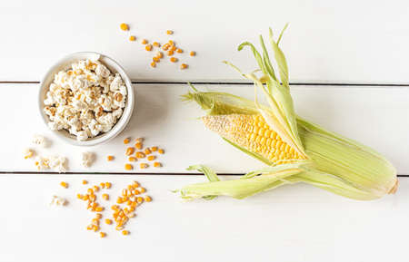 Popcorn, corn cob and corn grains, flat lay on a white wooden background. Concept of home-made munchies for a home party.の写真素材