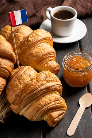 Fresh crispy French croissants, cup of coffee and orange jam served on a dark wooden background. Concept of a traditional French or continental breakfast.の写真素材