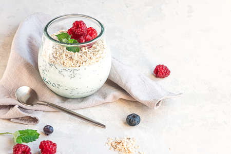 A glass with layered yogurt, chia seeds, oats and berries, gray concrete tabletop. Healthy breakfast, healthy lifestyle concept. Copy space.の写真素材