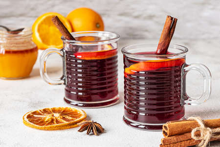 Two cups of hot mulled red wine with cinnamon sticks and orange. Spices, a jar of honey. Gray concrete background.の写真素材