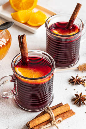 Two cups of hot mulled red wine with cinnamon sticks and orange. Spices, a jar of honey. Gray concrete background.の写真素材