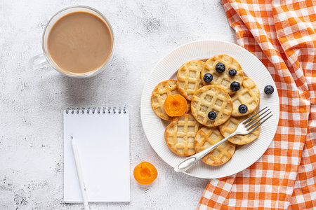 Small round waffles and a coffee on grey background, notebook, flat layの写真素材