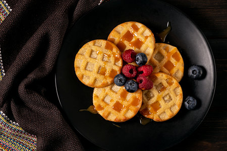 Small round waffles with berries on dark background, flat layの写真素材