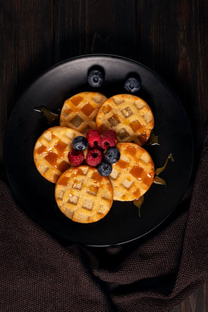 Small round waffles with berries on dark background, flat layの写真素材