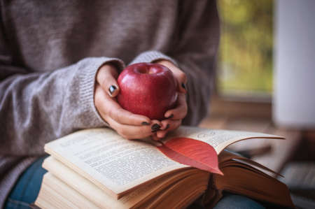 Young girl holding a red apple on a bookのeditorial素材