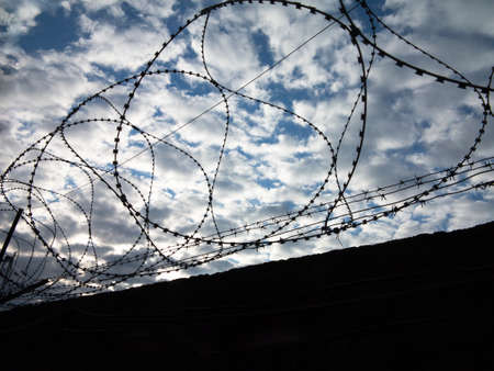 Thorned wire above concrete fence with fancy clouds on the backgroundの写真素材