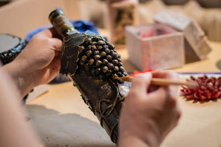 Female artist is using a painting brush on brown handmade bottle with leaves and grape made of coffee beansの写真素材
