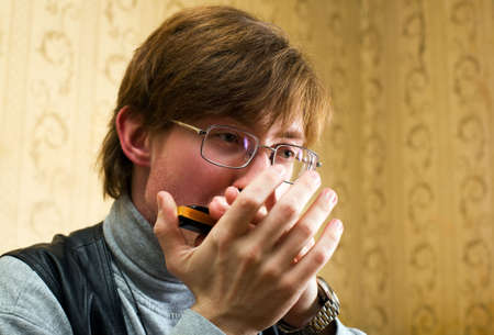 young man in glasses playing the harmonica