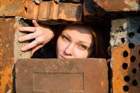 girl looking through a hole between bricksの写真素材