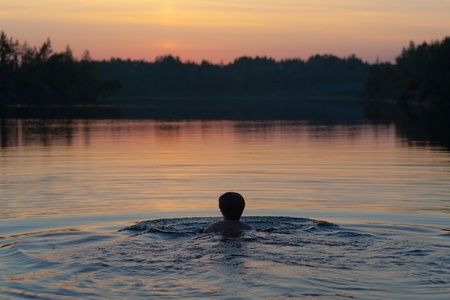 The woman swims in lake after sunsetの写真素材