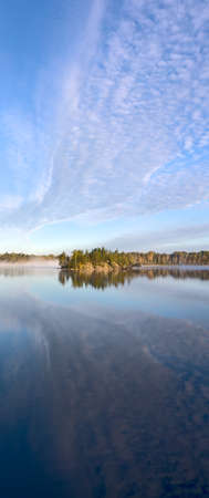 an island in the lake in the woods and the reflection of clouds