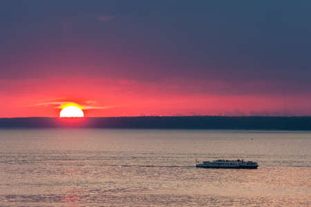 sun on the horizon at sunset and the ship on the waterの写真素材